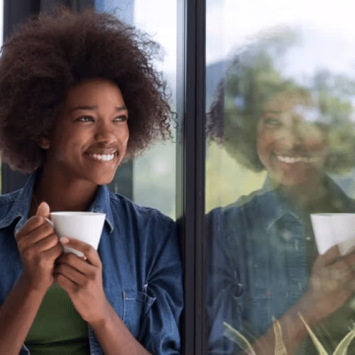 Person by glass window holding a coffee mug