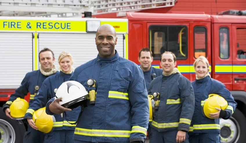 Firefighters standing in their emergency response uniforms outside of a firetruck. 