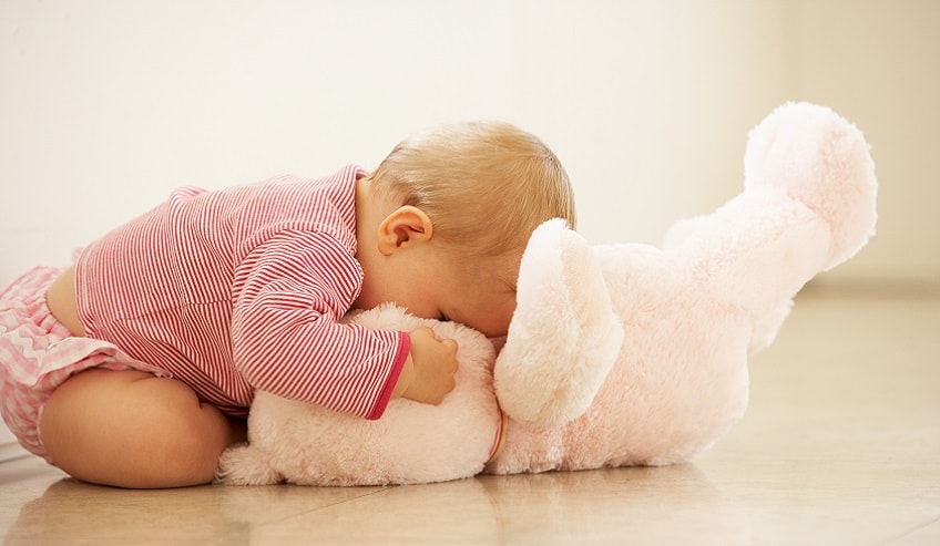 Baby in a diaper with its nose on a soft teddy bear.