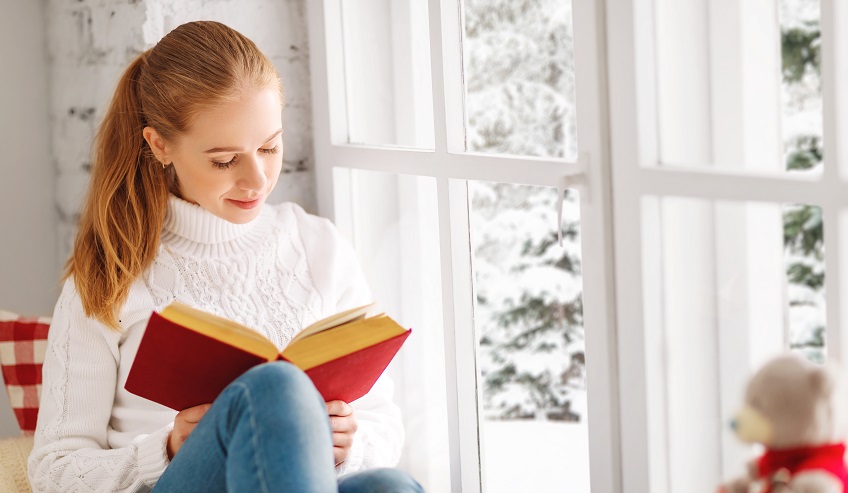 Woman reading a book by the window. 