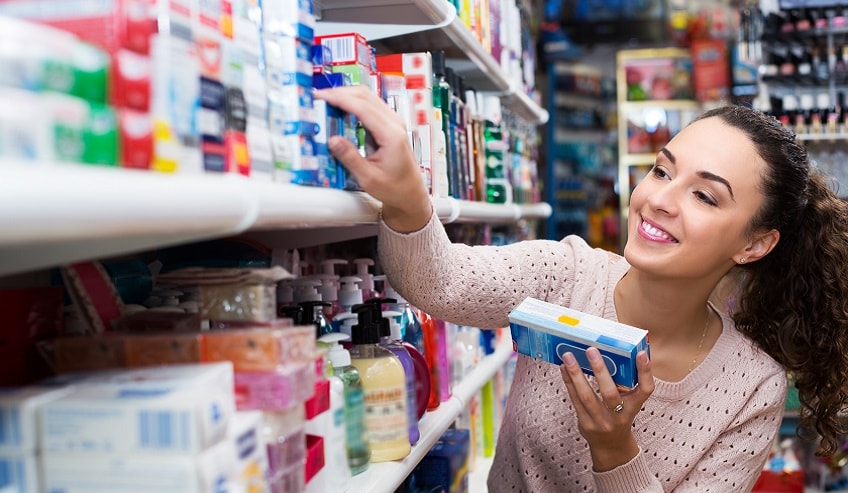 Lady reaching on a store shelf with many small boxes of product on it.
